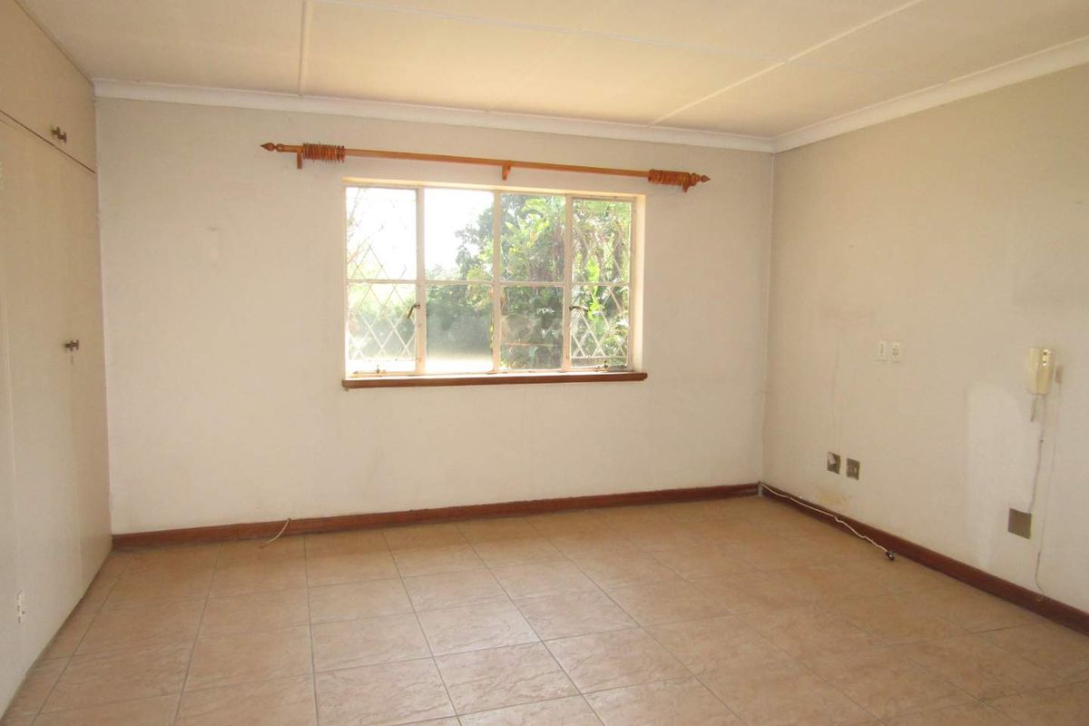 An empty bedroom featuring tiled flooring, a built-in cupboard, and a steel-framed window, offering a blank canvas for renovation.