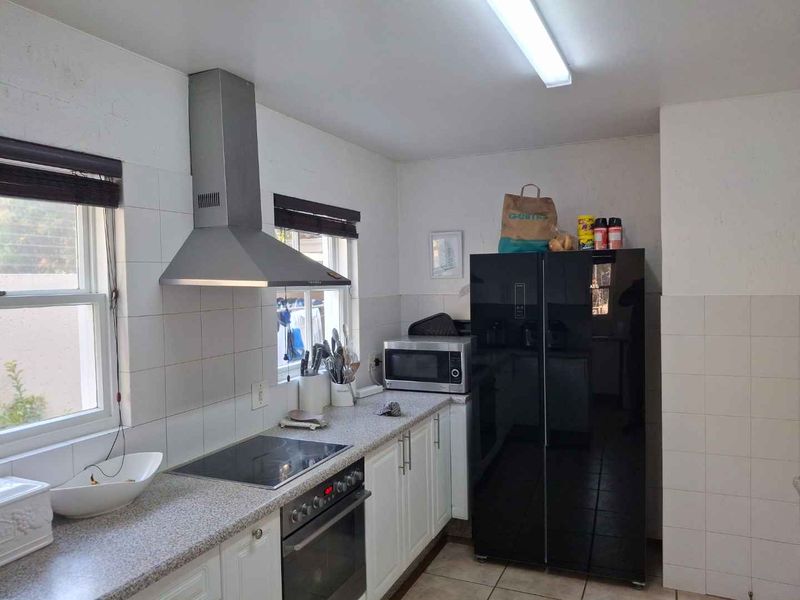 A functional kitchen featuring built-in cabinetry, a stainless steel extractor fan, electric hob, oven, and tiled backsplash with neutral finishes.