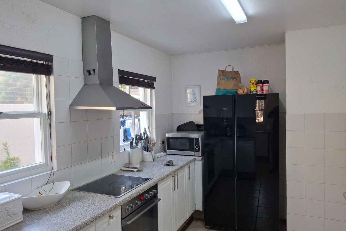 A functional kitchen featuring built-in cabinetry, a stainless steel extractor fan, electric hob, oven, and tiled backsplash with neutral finishes.