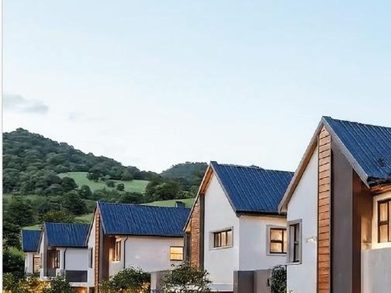 A row of modern townhouses featuring pitched metal roofs, timber accents, and clean stucco facades set against a scenic mountain backdrop.
