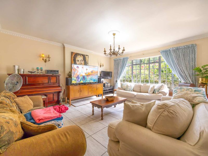 A spacious living room featuring tiled flooring, decorative ceiling coving, and a large steel-framed window that provides ample natural light.