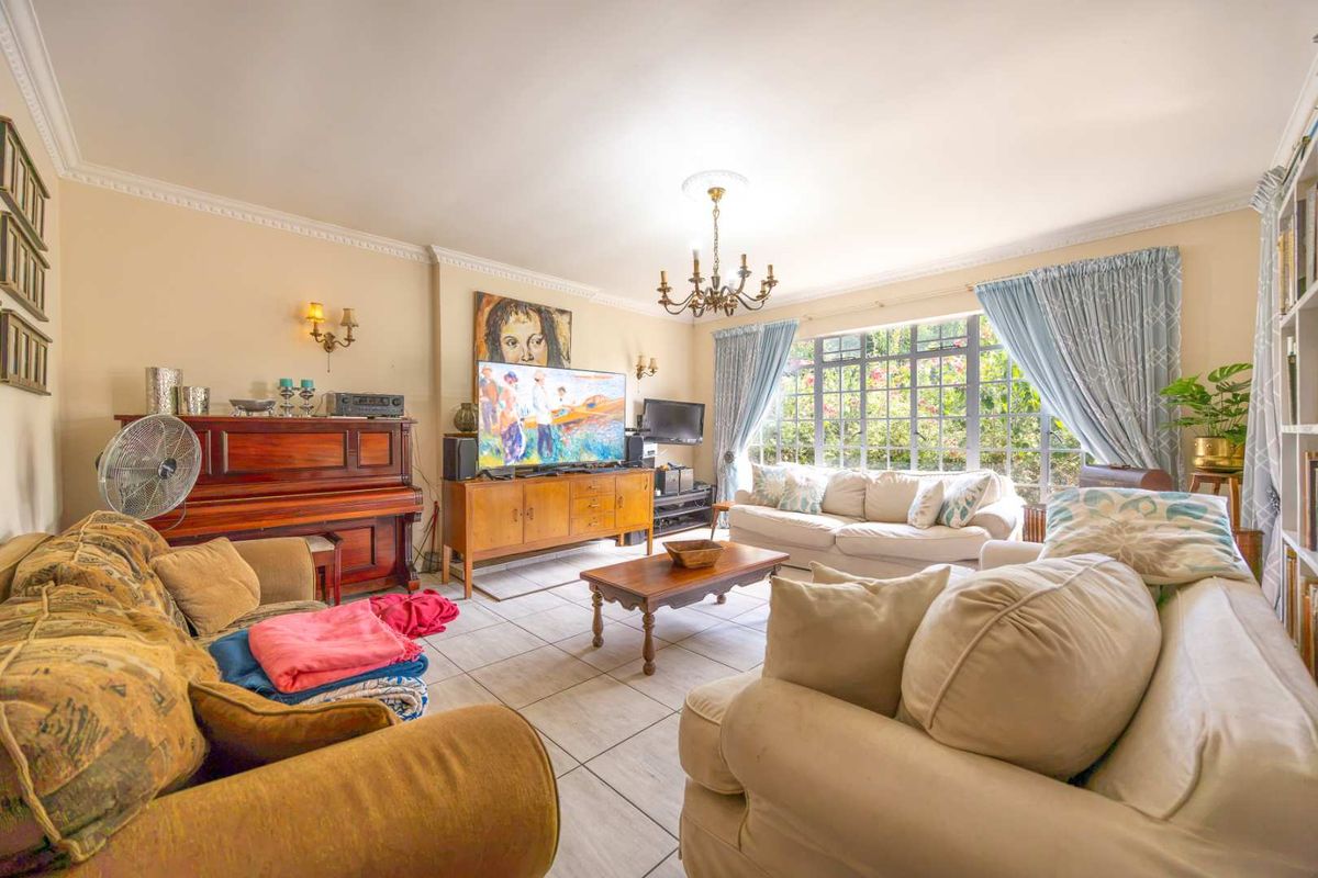 A spacious living room featuring tiled flooring, decorative ceiling coving, and a large steel-framed window that provides ample natural light.