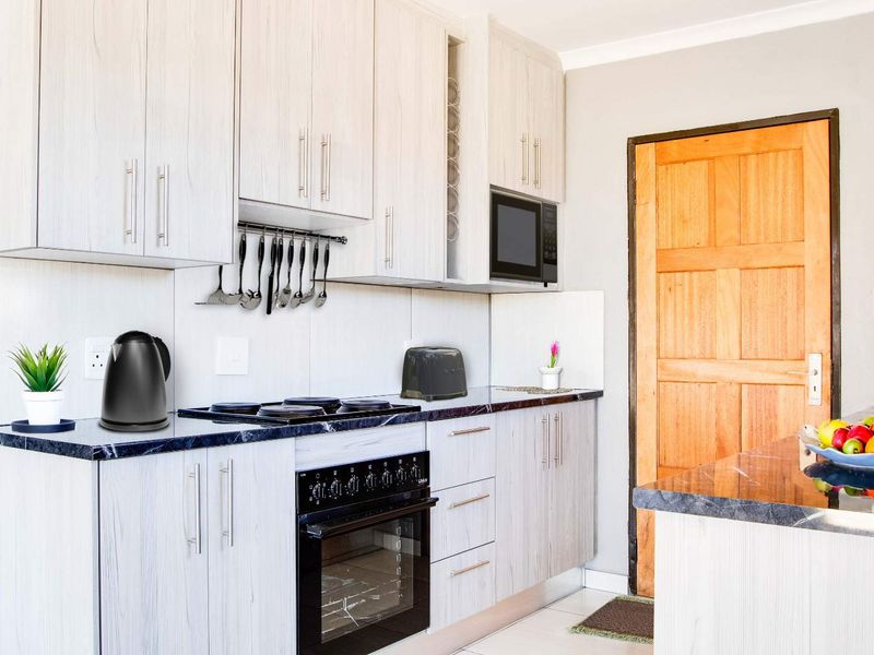 A functional kitchen featuring light wood-grain cabinetry, dark marble-effect countertops, built-in oven, hob, and microwave, with a convenient adjacent door access.