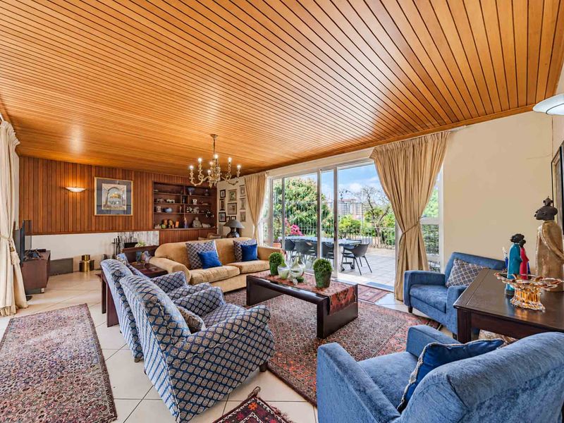 Spacious living room featuring warm timber-clad ceilings, wood wall paneling, built-in shelving, and large sliding glass doors providing access to the outdoor patio area.