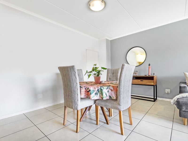 A bright living area featuring neutral tiled flooring, a grey accent wall, and clean finishes, providing a versatile space for dining or relaxation.