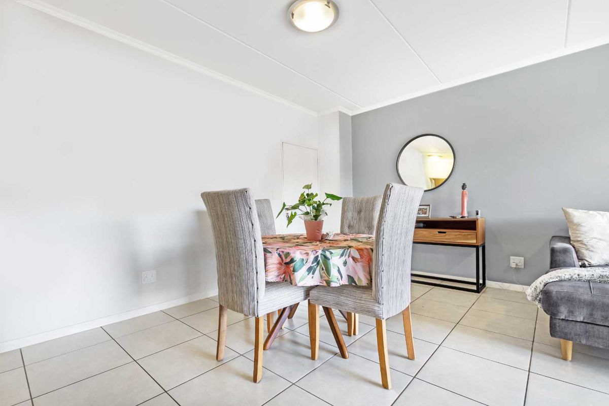 A bright living area featuring neutral tiled flooring, a grey accent wall, and clean finishes, providing a versatile space for dining or relaxation.
