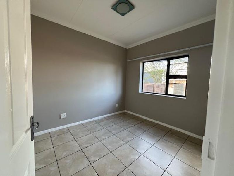 An empty bedroom featuring neutral wall paint, tiled flooring, and a window with a curtain rail, providing a clean and versatile living space.