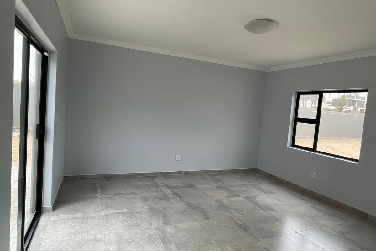 A bright, empty living room featuring large format floor tiles, modern black-framed windows, and sliding glass doors leading to the exterior.