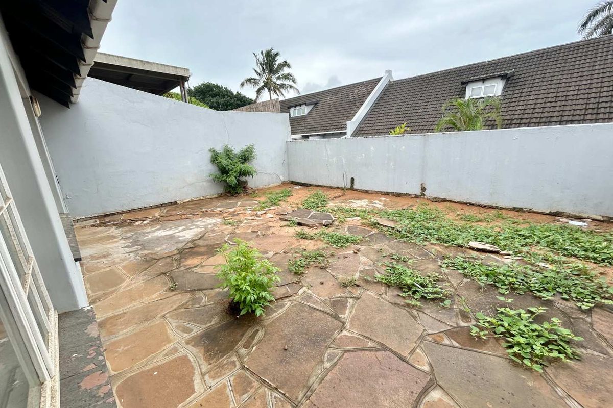 A private rear courtyard featuring stone paving, enclosed by boundary walls, requiring landscaping and maintenance to restore its outdoor living potential.