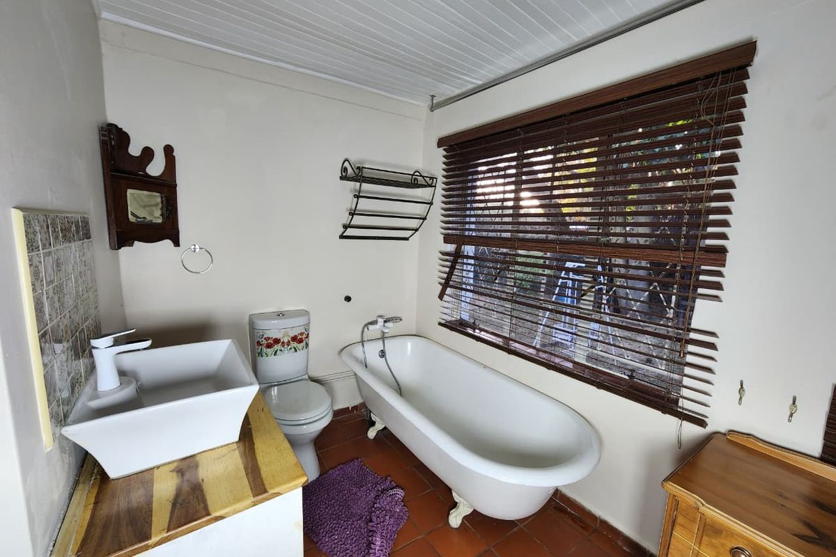 A bathroom featuring a classic clawfoot bathtub, a modern vessel sink on a timber vanity, and timber slat blinds.