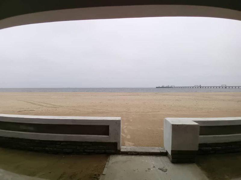 A direct view of the beach and ocean from a low-walled outdoor area, featuring a paved walkway leading toward the shoreline.