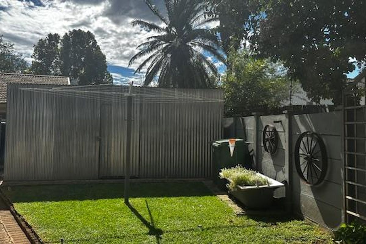 A private rear garden area featuring a lawn, a corrugated metal storage shed, and a perimeter boundary wall with decorative accents.
