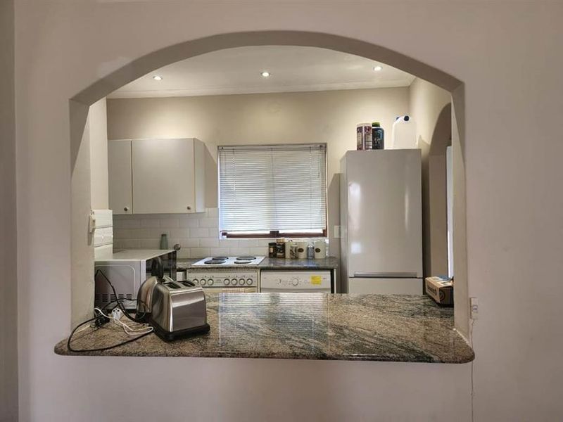 A functional kitchen featuring a granite breakfast bar, subway tile backsplash, and built-in cabinetry, viewed through a classic arched opening.