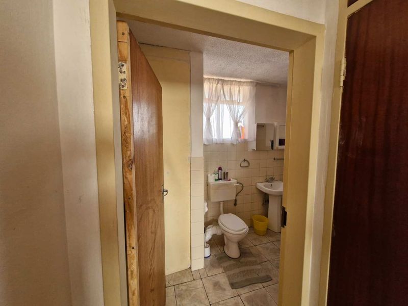 A functional bathroom featuring a pedestal basin, toilet, and tiled finishes, currently showing signs of age and wear.