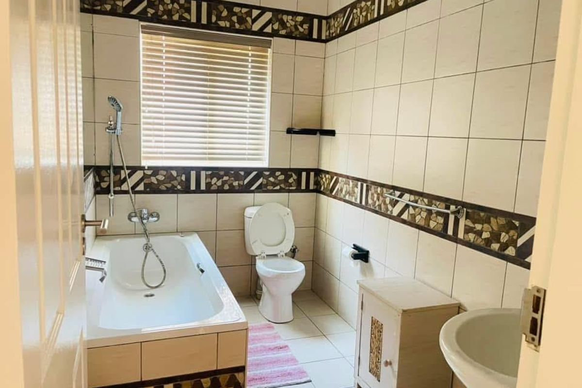 A functional bathroom featuring a built-in bathtub with shower attachment, a standard toilet, and a pedestal basin with tiled walls.
