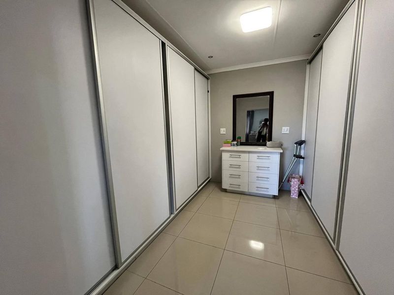 A well-maintained dressing area or bedroom featuring extensive built-in sliding door cupboards, neutral tiled flooring, and modern recessed ceiling lighting.