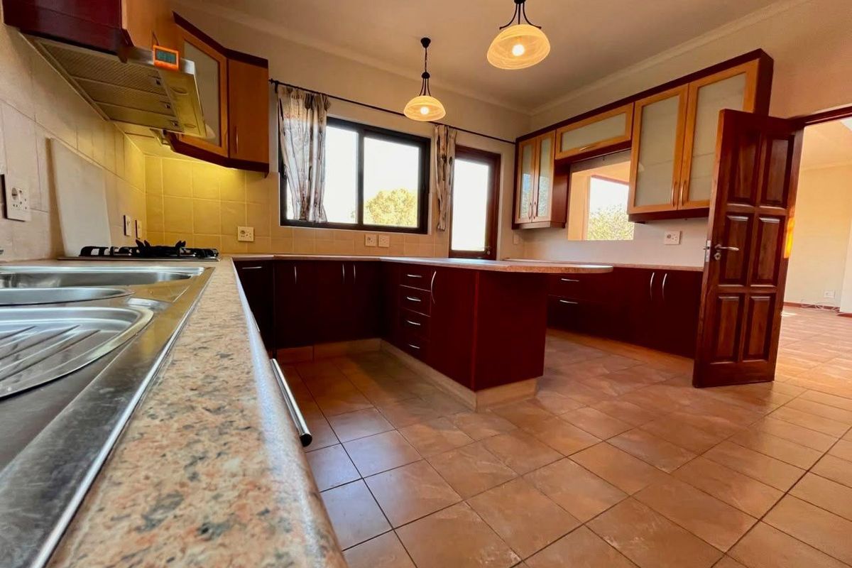 Spacious kitchen featuring dark wood cabinetry, laminate countertops, tiled flooring, and integrated gas hob with extractor fan, offering a functional layout.