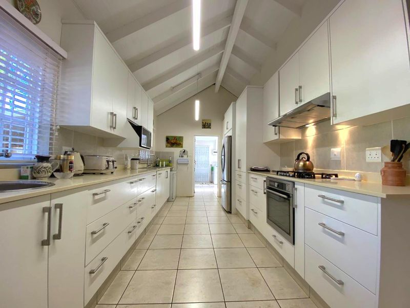 A well-lit galley kitchen featuring white cabinetry, stone countertops, built-in oven, gas hob, and a vaulted ceiling with tiled flooring.