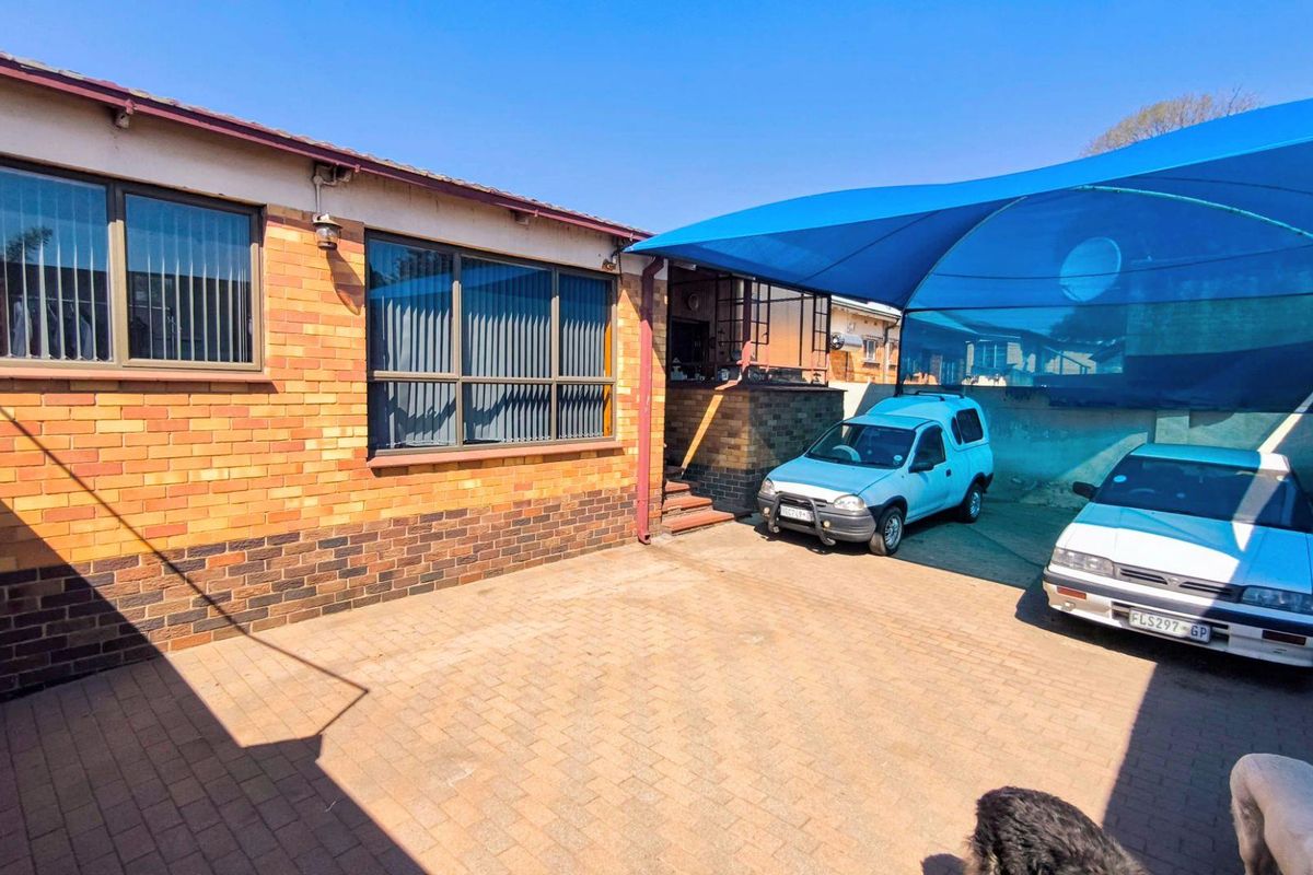 Rear exterior view of the property featuring a paved driveway, face brick walls, aluminium windows, and a large blue shade sail for vehicle protection.