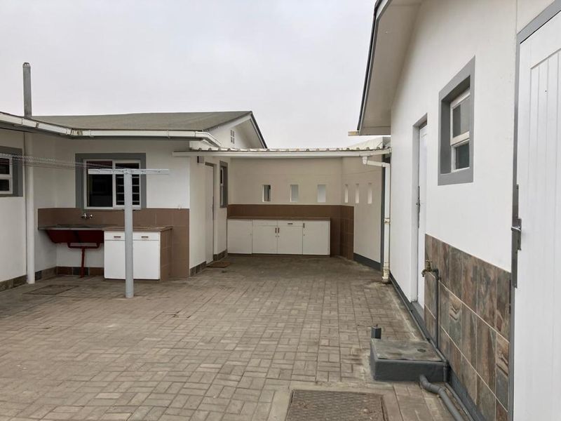 A paved rear courtyard featuring a covered utility area with built-in cabinetry, an outdoor sink, and functional drainage.