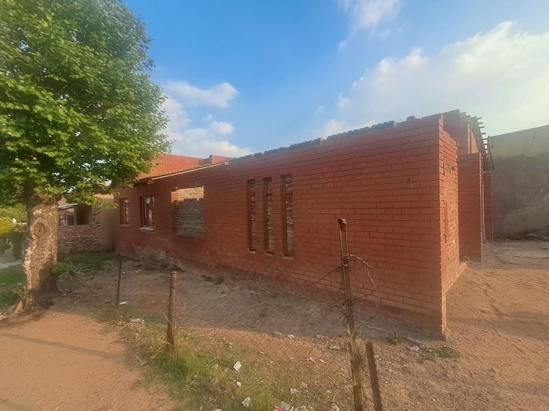 An exterior view of a residential property currently under construction, featuring exposed red brick walls and an incomplete structural frame.