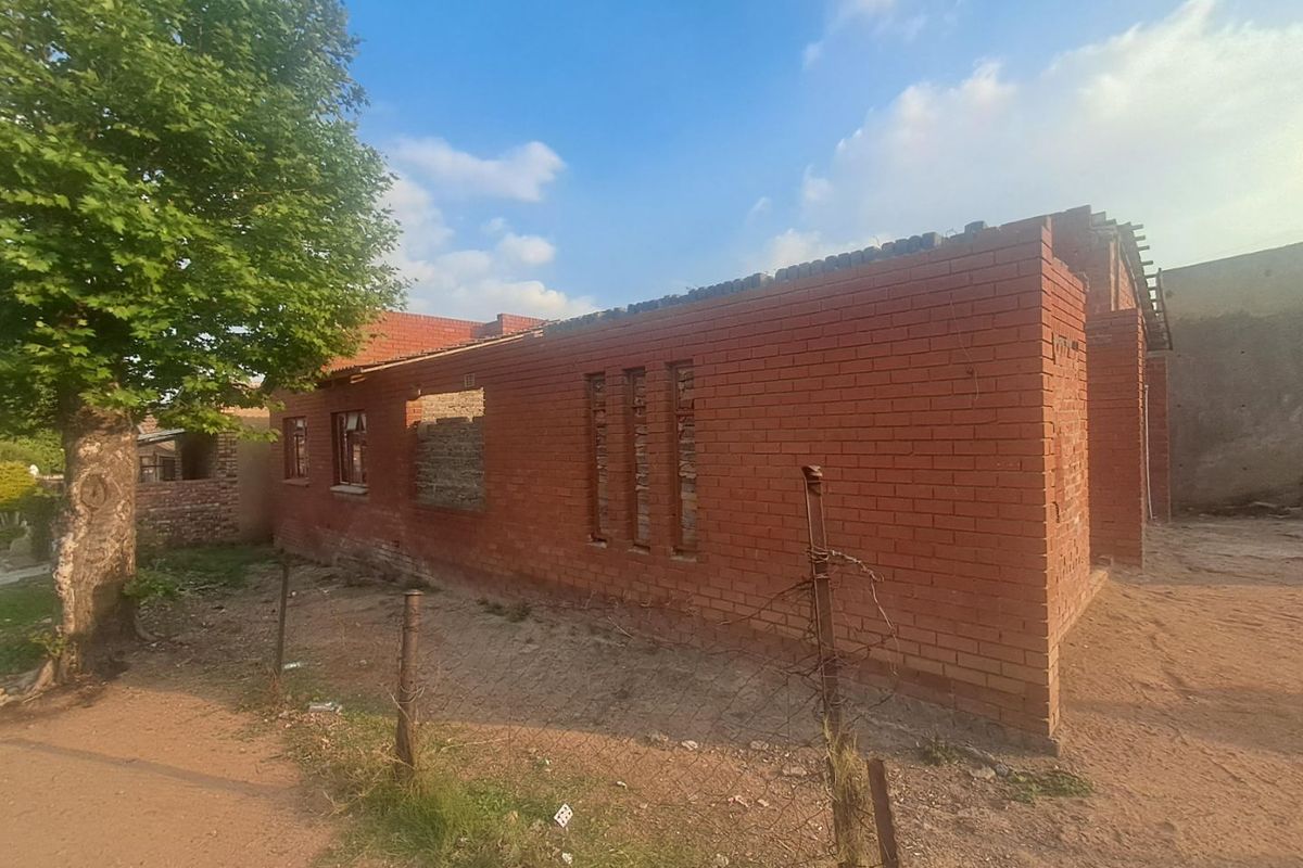 An exterior view of a residential property currently under construction, featuring exposed red brick walls and an incomplete structural frame.