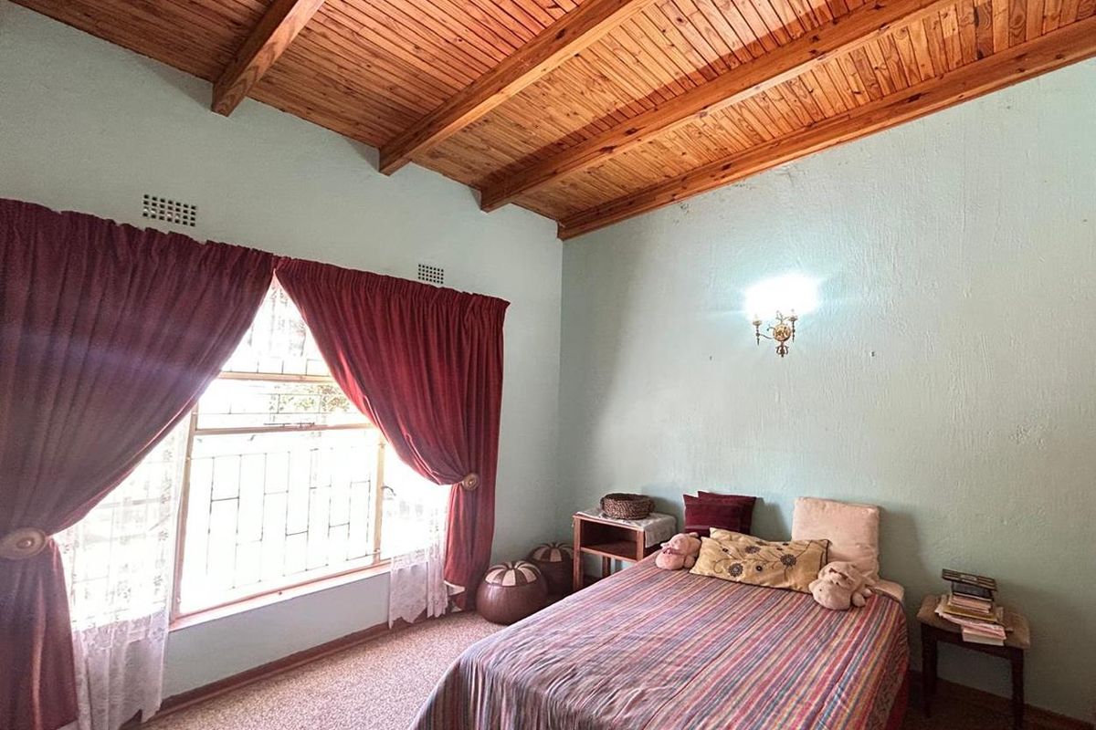 A bedroom featuring a vaulted timber-clad ceiling, carpeted flooring, and a large window with security bars.