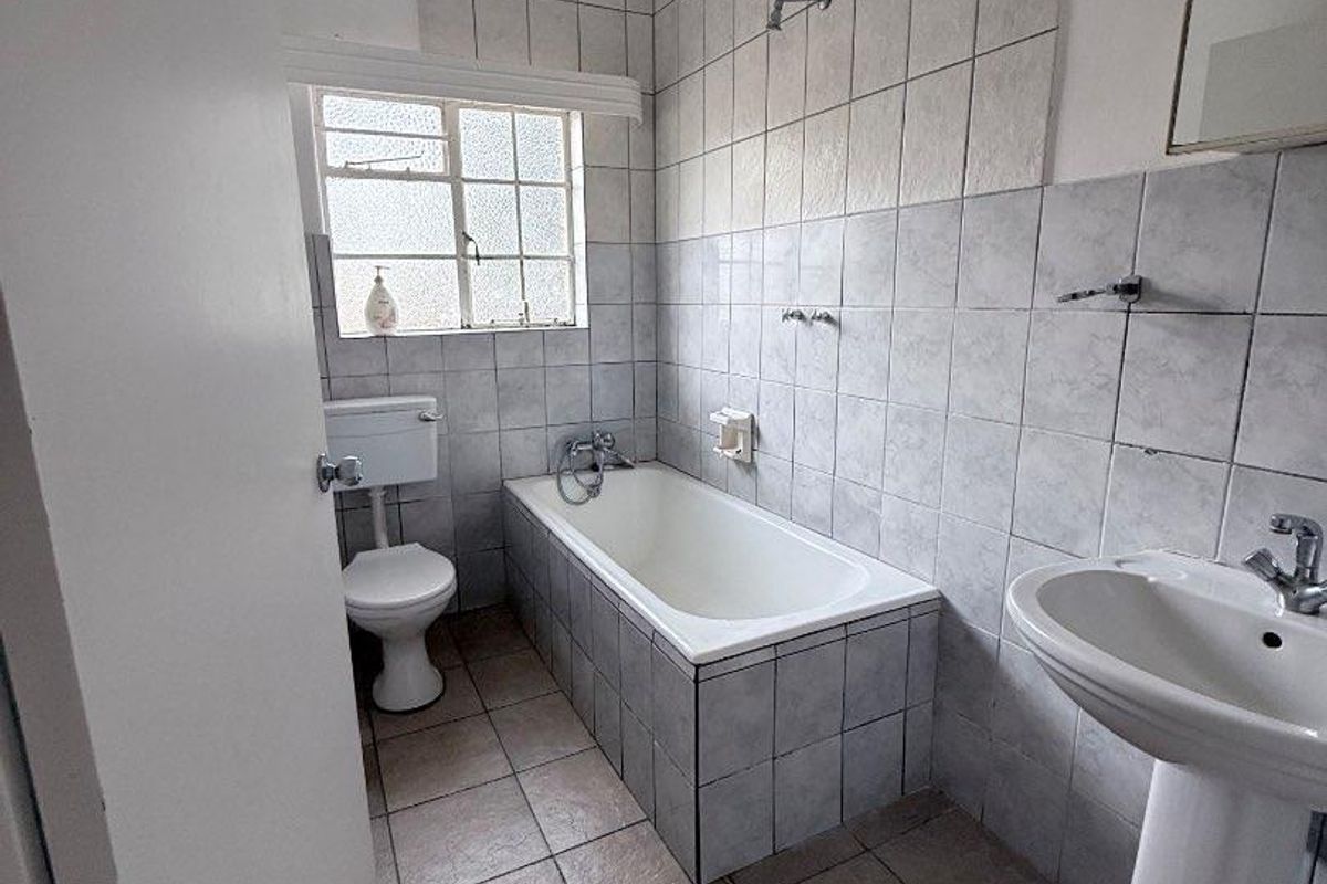 A functional bathroom featuring a pedestal basin, built-in bathtub, and wall-mounted shower, finished with ceramic tiling throughout.