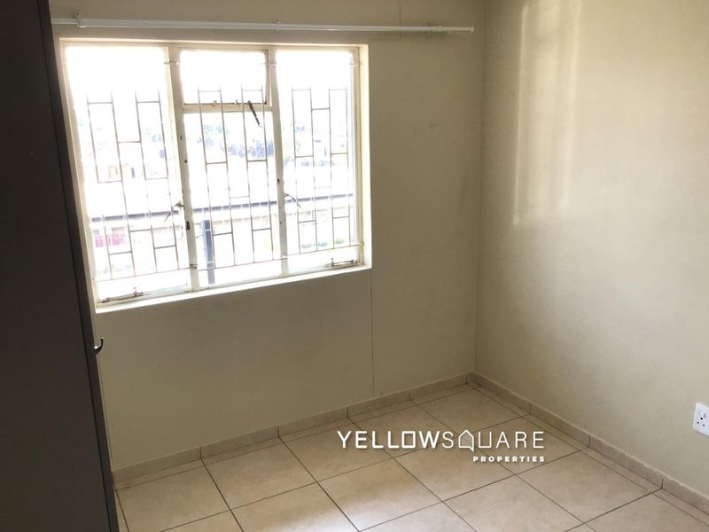 An empty bedroom featuring tiled flooring, a built-in cupboard, and a window fitted with security bars.