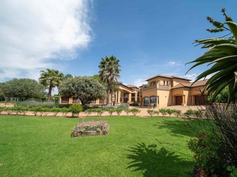 A spacious front elevation of a large residence featuring a paved driveway, manicured lawn, and established garden with mature trees.
