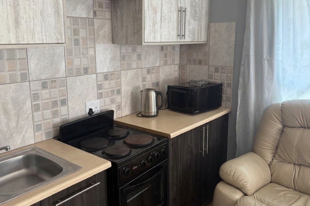 Compact kitchen featuring dark cabinetry, laminate countertops, a stainless steel sink, and a built-in electric stove with a decorative tiled backsplash.