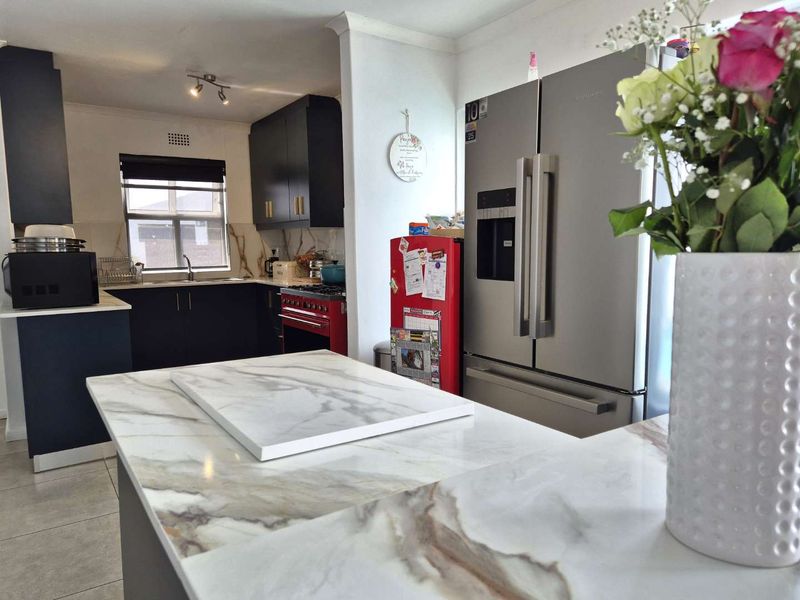 Modern kitchen featuring dark cabinetry, a marble-look island countertop, and tiled flooring, offering a functional and stylish culinary space.