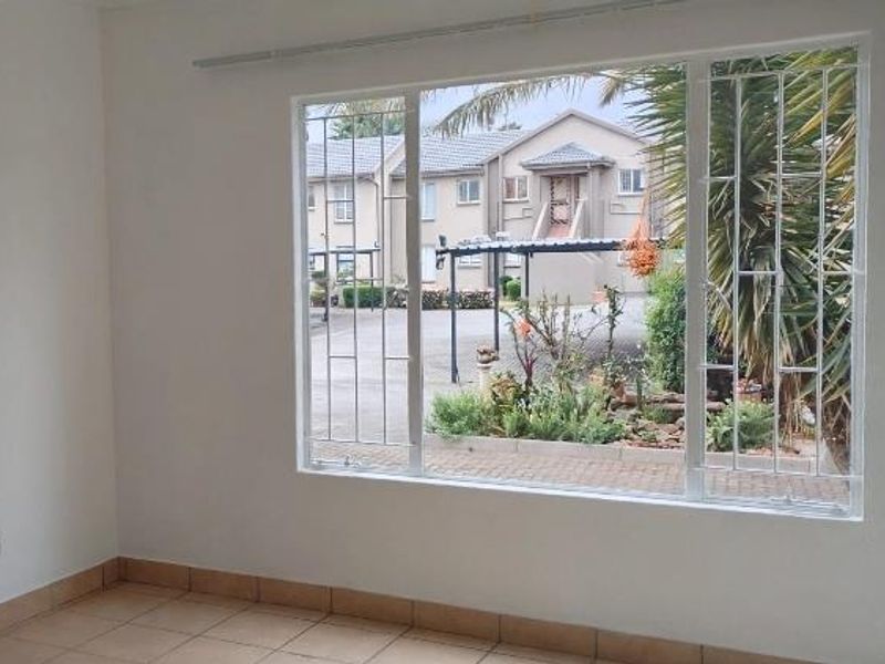 An empty living room featuring tiled flooring and a large window with security bars, offering a view of the complex exterior.