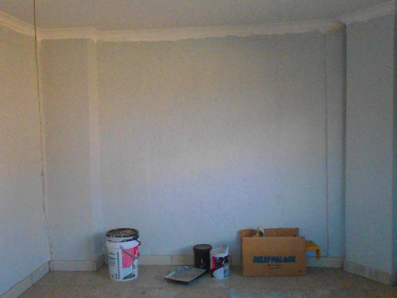 An empty room featuring tiled flooring and coved ceilings, currently undergoing minor maintenance or painting work.