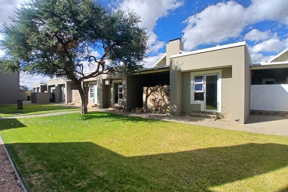 A view of the rear exterior of the townhouse, featuring a paved patio area, a well-maintained lawn, and a large mature tree.