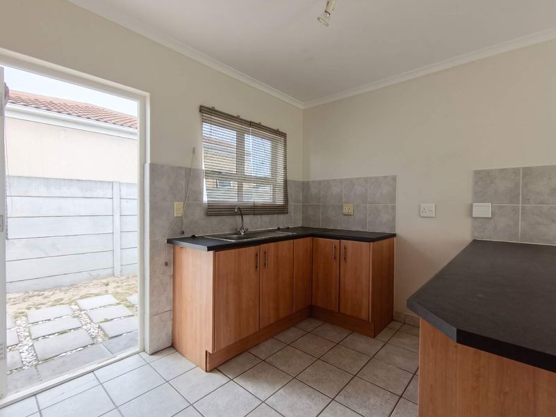 A functional kitchen featuring wood-finish cabinetry, dark laminate countertops, tiled flooring, and direct access to an outdoor patio area.