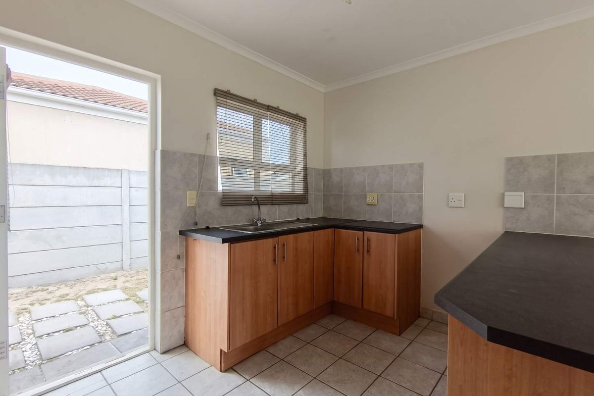 A functional kitchen featuring wood-finish cabinetry, dark laminate countertops, tiled flooring, and direct access to an outdoor patio area.