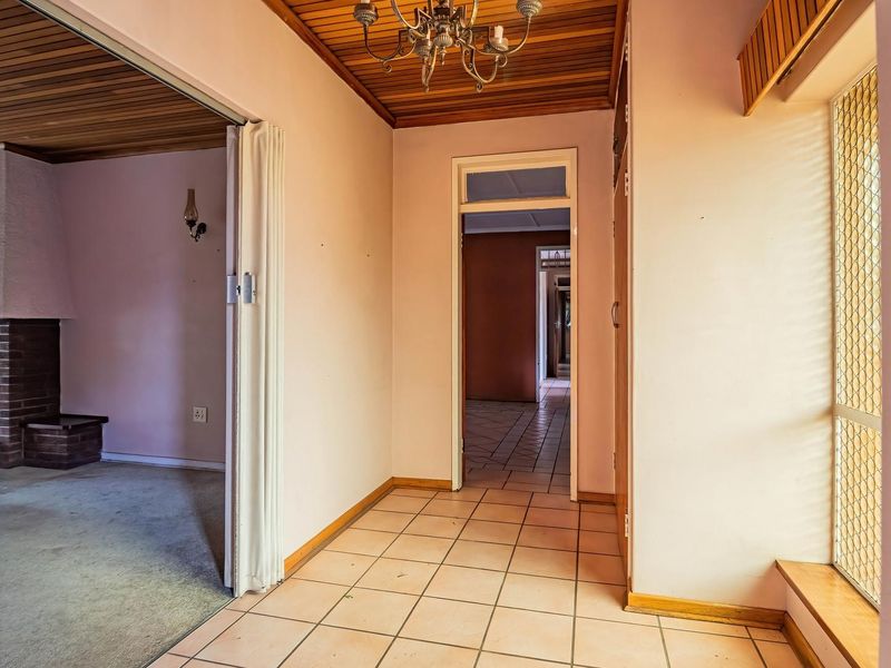 A spacious hallway featuring timber ceilings and tiled flooring, providing access to a living area with a brick fireplace and additional interior rooms.