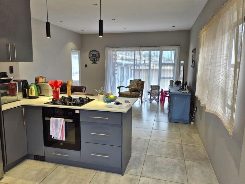Open-plan kitchen and living area featuring modern grey cabinetry, stone countertops, integrated gas hob and oven, tiled floors, and sliding doors to the exterior.