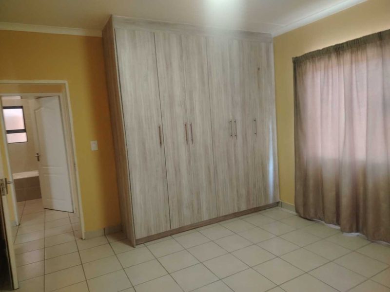A bedroom featuring light wood-finish built-in cupboards, neutral tiled flooring, and direct access to an adjoining bathroom.