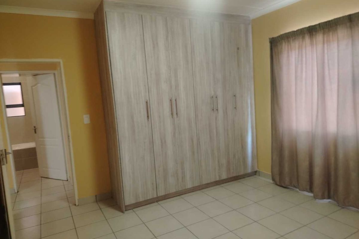 A bedroom featuring light wood-finish built-in cupboards, neutral tiled flooring, and direct access to an adjoining bathroom.