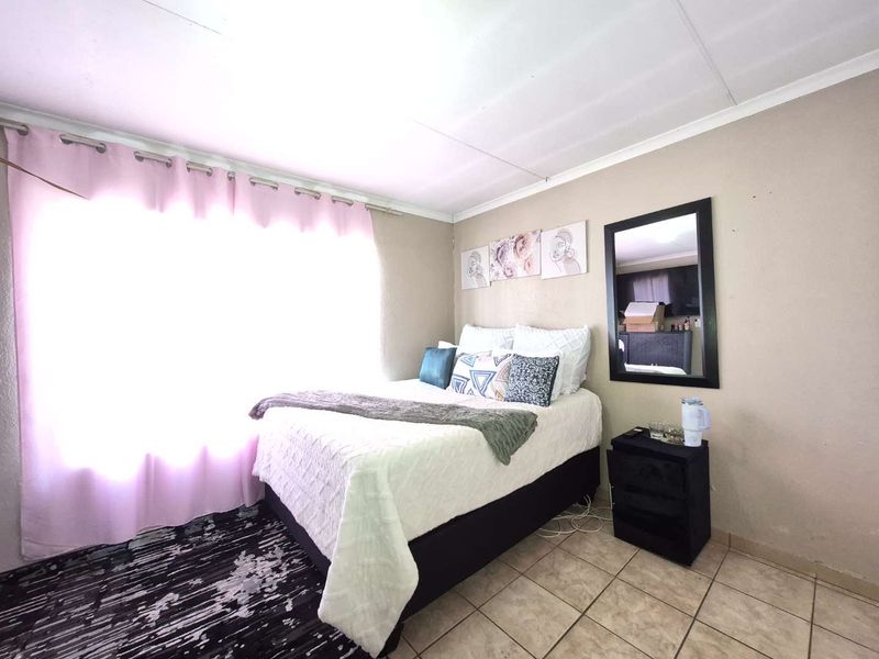 A functional bedroom featuring tiled flooring and large windows with curtain rails, providing a neutral base for personalization.