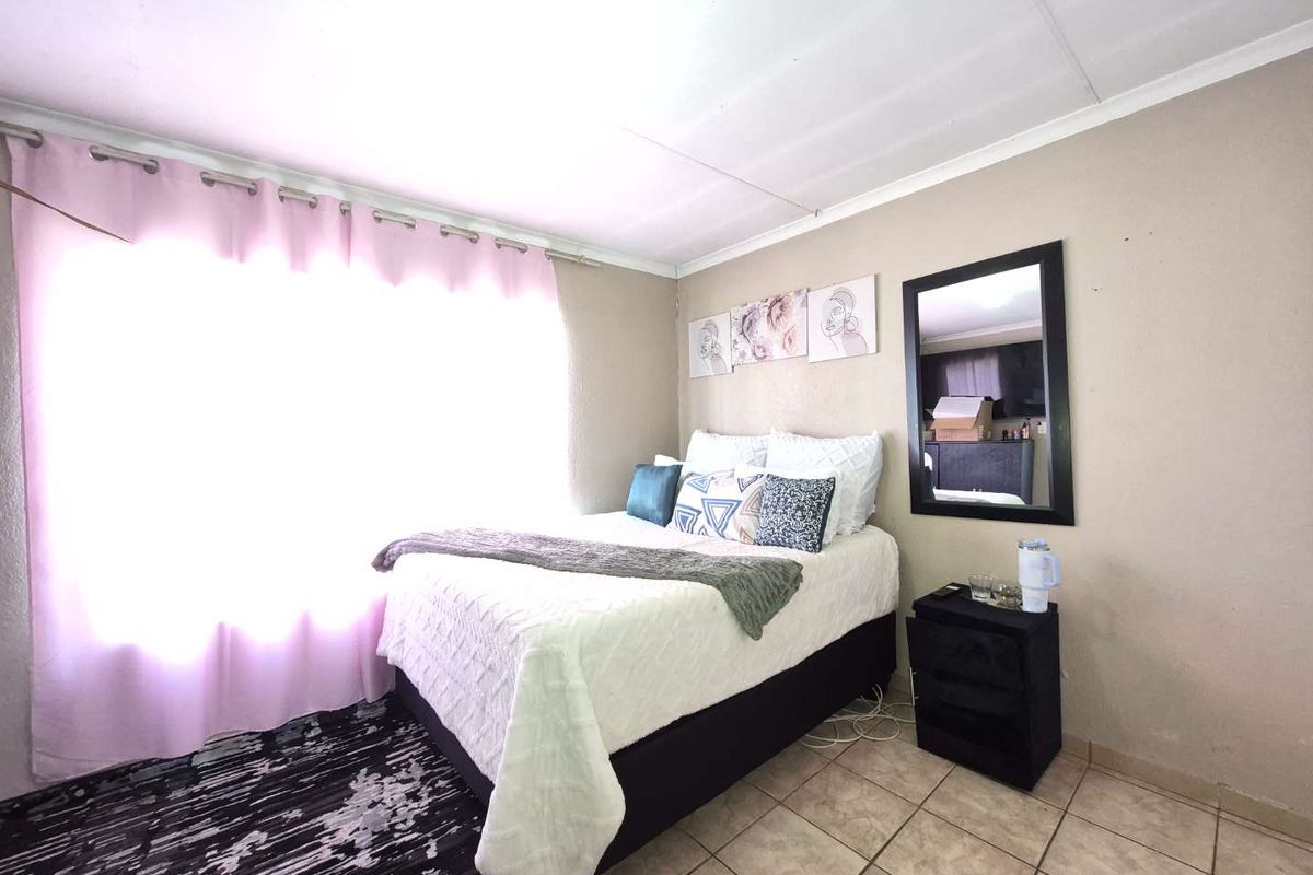 A functional bedroom featuring tiled flooring and large windows with curtain rails, providing a neutral base for personalization.