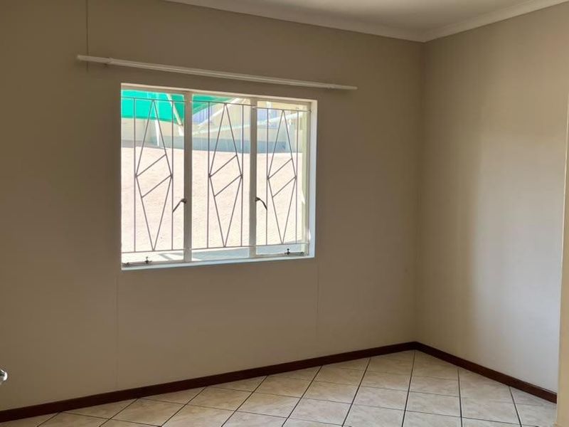 A clean, empty bedroom featuring neutral walls, tiled flooring, and a window fitted with security bars.