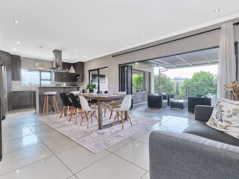 Spacious open-plan living and dining area featuring a modern kitchen with island, flowing seamlessly through stacking doors to a covered outdoor patio.