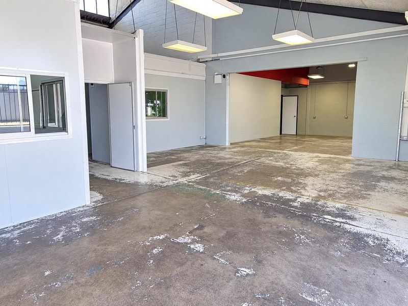 Spacious industrial utility area featuring exposed ceiling beams, suspended lighting, and durable concrete flooring, suitable for various commercial or workshop applications.