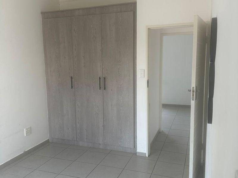 A clean, empty bedroom featuring neutral tiled flooring and modern built-in cupboards with a light wood finish.
