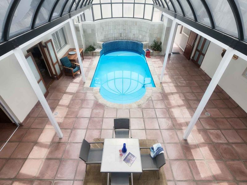 An indoor swimming pool area featuring a glass conservatory roof, tiled flooring, and a tiled pool surround, providing a bright and protected swimming space.