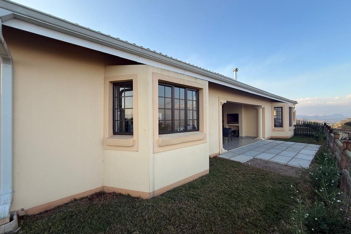 Rear view of the townhouse featuring a paved patio area, built-in braai, and bay windows overlooking the surrounding landscape.