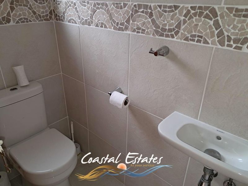 A clean and functional guest bathroom featuring neutral wall tiles, a decorative mosaic border, a wall-mounted basin, and a modern toilet.